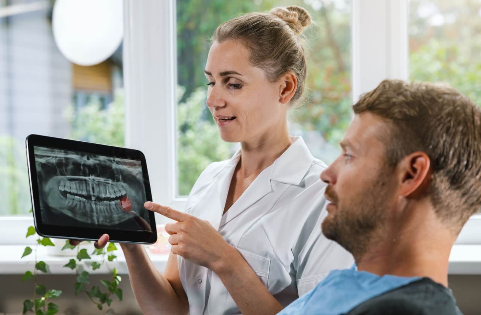 Dentist showing a dental X-ray on a tablet to a patient, pointing to a wisdom tooth.