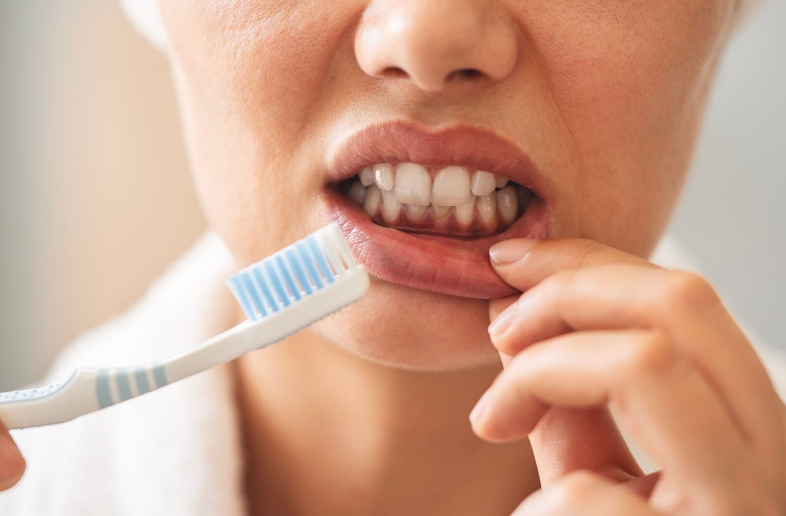 A person holds a manual toothbrush next to their lip and natural teeth.