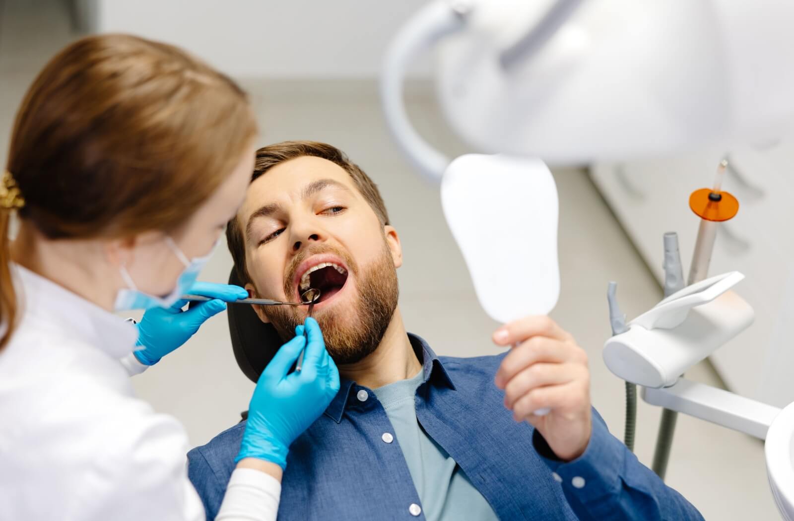 A man receiving a dental checkup from a hygienist while holding a mirror.